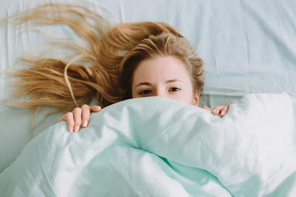 Frau im Bett und das halbe Gesicht unter einer Bettwäsche versteckt — Stockfoto