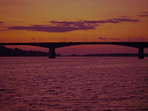 Gün batımında bir nehir üzerinde su üzerinde bir köprü siluet, citysc — Stok fotoğraf