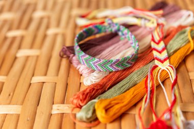 Parlak pamuk ipliklerden örülmüş, nakış işlemek için renkli iplikler ve rattan bir masanın üzerine örülmüş. Seçici odaklanma. Hobiler, geleneksel sanat, boho tarzı mücevherler, hippiler. El yapımı.