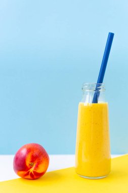Kokteyl olarak bir kavanozda parlak sarı zerdeçal kokteyli, sarı, gökyüzü mavisi arka planda olgun nektarin. Sağlıklı beslenme, vejetaryenlik, detoksin. Kahvaltı içeceği. Plastiğin reddedilmesi..