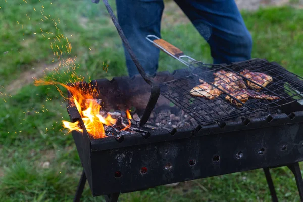 Meat is grilled. A man stirring coals with a hot poker. Sparks fly from fire in grill. Outdoor cooking. Picnic, weekend