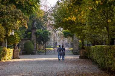 Young couple walking in the middle of an autumn path towards the castle gate of Grazzano Visconti, Piacenza, Italy clipart