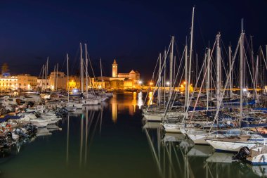 Night view of Trani harbor in Apulia, Italy, with yachts, reflections, and illuminated cathedral. Idyllic Mediterranean seascape for travel and lifestyle imagery