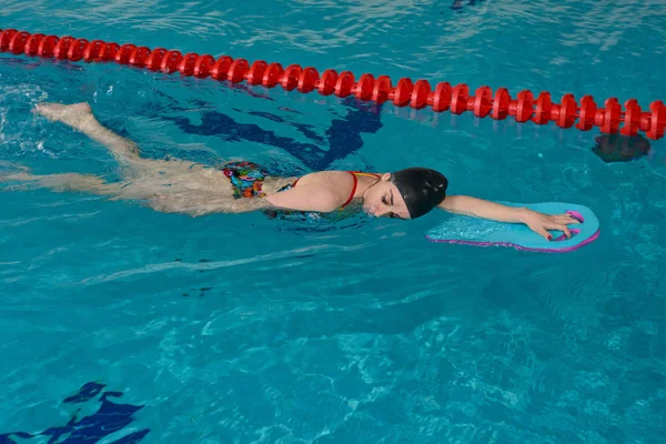 一个年轻的女孩在泳池里游泳 用支撑板在赛道表面练习平滑的运动 — 图库照片