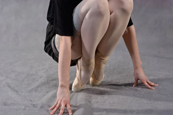 Closeup of a ballerina\'s feet in pointe shoes on grey background. Classical school of ballet.