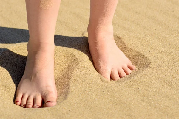 Women\'s feet close up on the clean beach sand, filmed from close up on a Sunny day. Foot skin care.