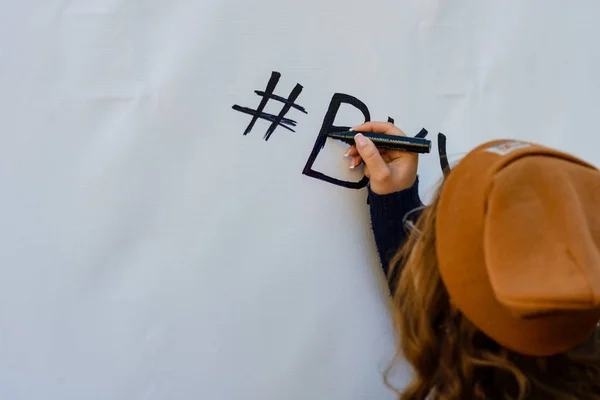The girl writes black marker on white wall the sign hashtag and main letter of the word