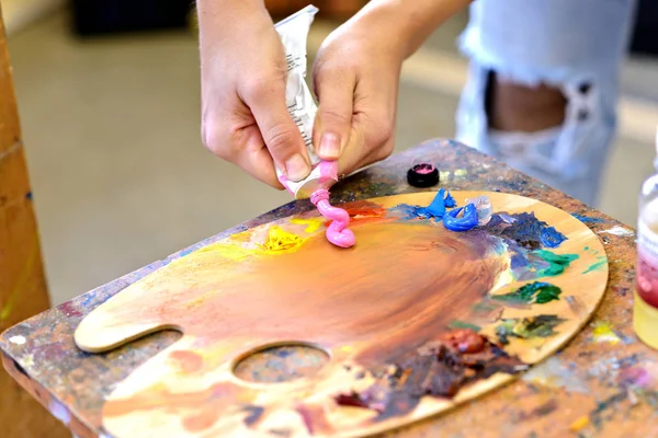 The artist's hands squeeze the paint from the tube on the prepared palette.