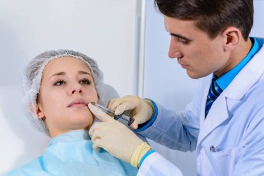 Kozmetik uzmanının elleri yüzüne ve dudaklarına iğne yapıyor. Genç bir kadın güzellik salonunda yüz aşısı yaptırıyor. Yaşlanma, gençleşme ve hidrasyon prosedürleriyle yüzleş. Estetik kozmetoloji. Kapat..