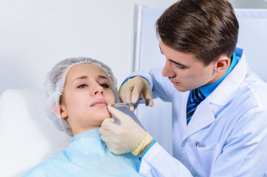 Kozmetik uzmanının elleri yüzüne ve dudaklarına iğne yapıyor. Genç bir kadın güzellik salonunda yüz aşısı yaptırıyor. Yaşlanma, gençleşme ve hidrasyon prosedürleriyle yüzleş. Estetik kozmetoloji. Kapat..