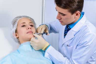 Kozmetik uzmanının elleri yüzüne ve dudaklarına iğne yapıyor. Genç bir kadın güzellik salonunda yüz aşısı yaptırıyor. Yaşlanma, gençleşme ve hidrasyon prosedürleriyle yüzleş. Estetik kozmetoloji. Kapat..