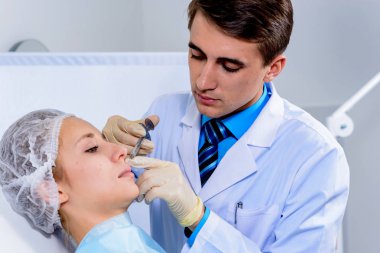 Kozmetik uzmanının elleri yüzüne ve dudaklarına iğne yapıyor. Genç bir kadın güzellik salonunda yüz aşısı yaptırıyor. Yaşlanma, gençleşme ve hidrasyon prosedürleriyle yüzleş. Estetik kozmetoloji. Kapat..