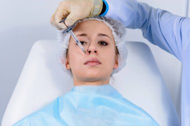 Kozmetik uzmanının elleri yüzüne ve dudaklarına iğne yapıyor. Genç bir kadın güzellik salonunda yüz aşısı yaptırıyor. Yaşlanma, gençleşme ve hidrasyon prosedürleriyle yüzleş. Estetik kozmetoloji. Kapat..