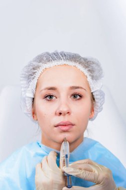 Kozmetik uzmanının elleri yüzüne ve dudaklarına iğne yapıyor. Genç bir kadın güzellik salonunda yüz aşısı yaptırıyor. Yaşlanma, gençleşme ve hidrasyon prosedürleriyle yüzleş. Estetik kozmetoloji. Kapat..