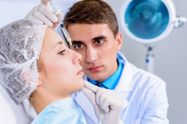 Kozmetik uzmanının elleri yüzüne ve dudaklarına iğne yapıyor. Genç bir kadın güzellik salonunda yüz aşısı yaptırıyor. Yaşlanma, gençleşme ve hidrasyon prosedürleriyle yüzleş. Estetik kozmetoloji. Kapat..