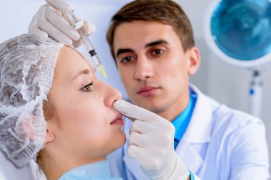 Kozmetik uzmanının elleri yüzüne ve dudaklarına iğne yapıyor. Genç bir kadın güzellik salonunda yüz aşısı yaptırıyor. Yaşlanma, gençleşme ve hidrasyon prosedürleriyle yüzleş. Estetik kozmetoloji. Kapat..