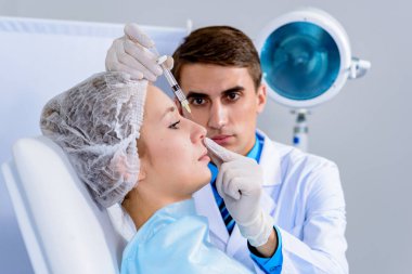 Kozmetik uzmanının elleri yüzüne ve dudaklarına iğne yapıyor. Genç bir kadın güzellik salonunda yüz aşısı yaptırıyor. Yaşlanma, gençleşme ve hidrasyon prosedürleriyle yüzleş. Estetik kozmetoloji. Kapat..