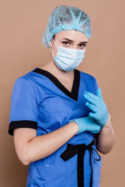 Başında koruyucu bir başlık ve şeftali arkaplanda mavi eldivenler olan cerrahi üniformalı genç bir doktor..