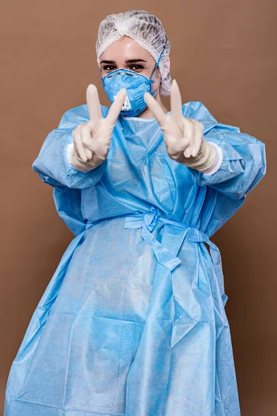 A medical worker in a surgical, disposable suit, respirator and gloves, playfully shows the victory sign, twice.