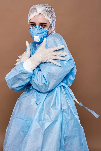 A medical worker in a surgical, disposable suit, respirator and gloves, playfully covers up as if hiding nudity.