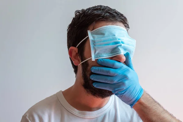 Sakallı ve maskeli bir erkek, gözlerini tarafsız bir geçmişle kapatıyor. Coronavirus krizinin kavramsal görüntüsü