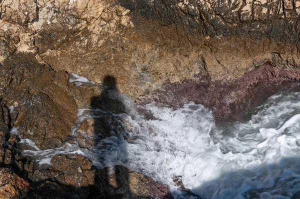 Shadow of a person projected on a background of rocks and waves of the coast of the island of Mallorca, Mediterranean Sea, Spain