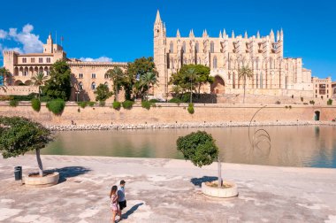 Palma de Mallorca, Balearic Adaları / İspanya; Eylül 2020: Parc de la Mar. Arka planda Palma Katedrali ve Almudaina Sarayı. Ön planda maskeli iki turist var.
