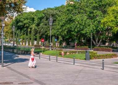 Palma de Mallorca, Balearic Adaları / İspanya; Eylül 2020: akıllı telefonuna ve maskesine bakan açık renk elbiseli kadın, Palma de Mallorca 'da güneşli bir caddede tek başına yürüyor.
