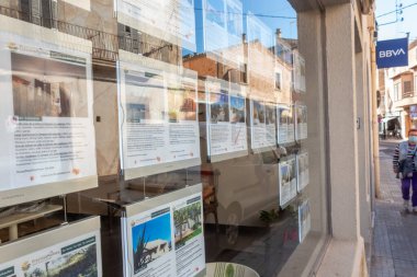 Campos, Balear Adaları / İspanya; Ekim 2020: bir emlak acentesinin sergilenmesi. Arka planda, yüzü maskeli yaşlı bir kadın caddede yürüyor. Yeni normallik kavramı