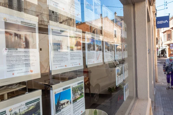 Campos, Balear Adaları / İspanya; Ekim 2020: bir emlak acentesinin sergilenmesi. Arka planda, yüzü maskeli yaşlı bir kadın caddede yürüyor. Yeni normallik kavramı