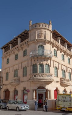 Campos, Balear Adaları / İspanya; Ekim 2020: bir bankaya ev sahipliği yapan tarihi bina. Girişte kişisel güvenlik zırhlı bir araca para taşıyor. İnsanlar yeni sağlık önlemlerini bekliyor.