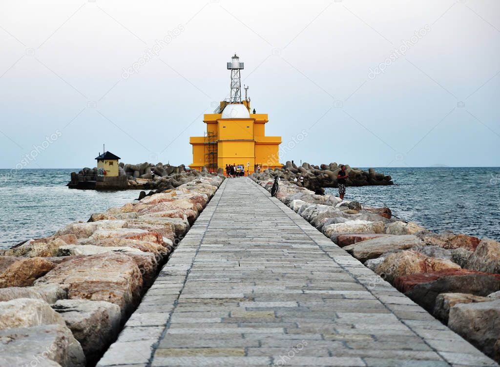 Italy, beautiful yellow lighthouse by the Mediterranean sea, stone pier with fishermen