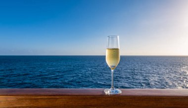 Yolcu gemisinin ahşap korkuluklarında bir bardak köpüklü beyaz şarap. Yaz tatilinde alkollü içki.