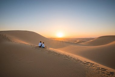Çöl manzarası. Genç bir çift gün batımını seyrediyor..
