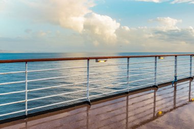 Yağmurlu bir günde korkuluklu ve ışıklı ıslak bir gemi güvertesi. Arka planda beyaz bulutlar ve deniz.