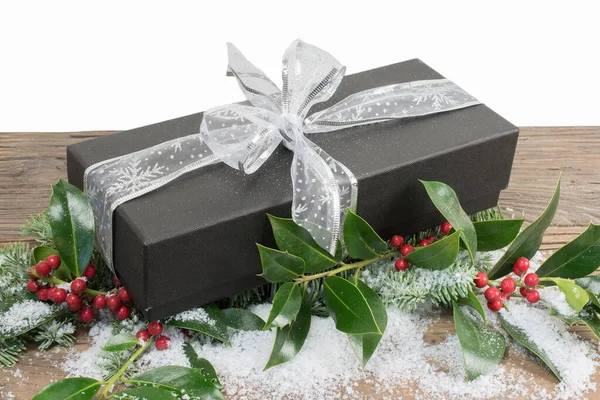 Black luxury gift box with silver ribbon on a wooden table with decorative holly and snow.Christmas and New Years gift.