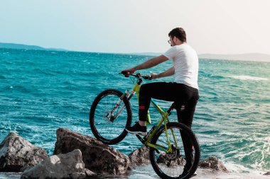 Hırvatistan 'ın Split kentinde, Mayıs 2020' de bir plaj kayasına yaslanmış bir bisikletle kıyıda duran genç adam. Rüzgârlı bir günde kıyıya vuran dalgalar onu ve çevreyi su baskınına uğratır.