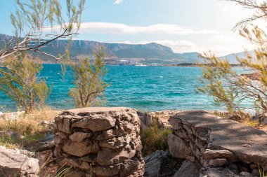 Eski taş ve sandalyeler küçük bir körfezde saklanmış taşlardan yapılmış, ikiye bölünmüş, Hırvat. Sıcak bir yaz günü. Sırt çantasındaki berrak deniz. Tropik seyahat cenneti