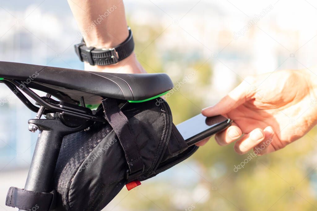 Man putting his smartphone inside a small black pouch for storage under the seat of a bicycle
