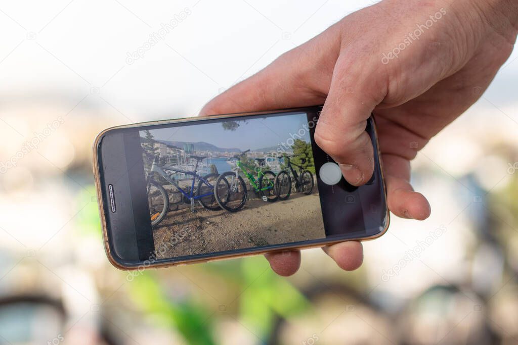Hand holding a smartphone taking a photo of a couple of bicycles standing leaned on a wall