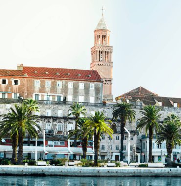 Hırvatistan 'ın Split kentinden Riviera. Kıyıdaki yeşil güzel palmiye ağaçları. Aziz Sahip 'in eski çan kulesi eski şehir binalarını gözetliyor. Öndeki mavi deniz