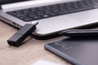 Siyah grafik tableti gümüş bir dizüstü bilgisayarın önünde. Usb sürücüsü dizüstü bilgisayara dayanıyor. Grafik tasarımcısı, çizer tablosu