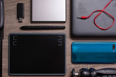 Modern teknoloji ve fotoğraf düz gri ahşap masa üzerinde yatıyordu. Mavi akıllı telefon, kırmızı kablolu gri laptop, grafik tableti, kamera tripodu, usb çubuğu.