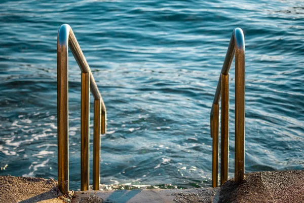 Steel reflecting silver stairs leading into a beautiful blue sea. Open sea beach of the adriatic sea in croatia