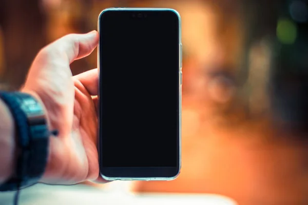 Elinde boş bir akıllı telefon, elinde mavi bir kol saati var. Odak dışı bulanık turuncu arkaplan