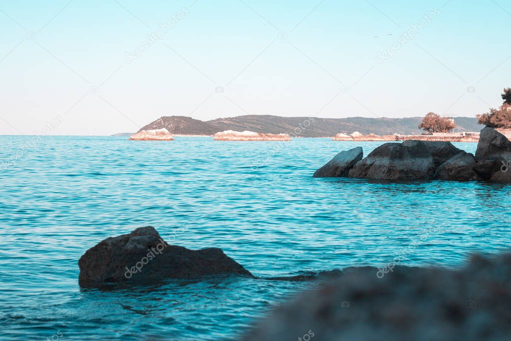 Rocky shore of split, croatia. Multiple rocks in the beautiful blue sea. Island shore in the distance