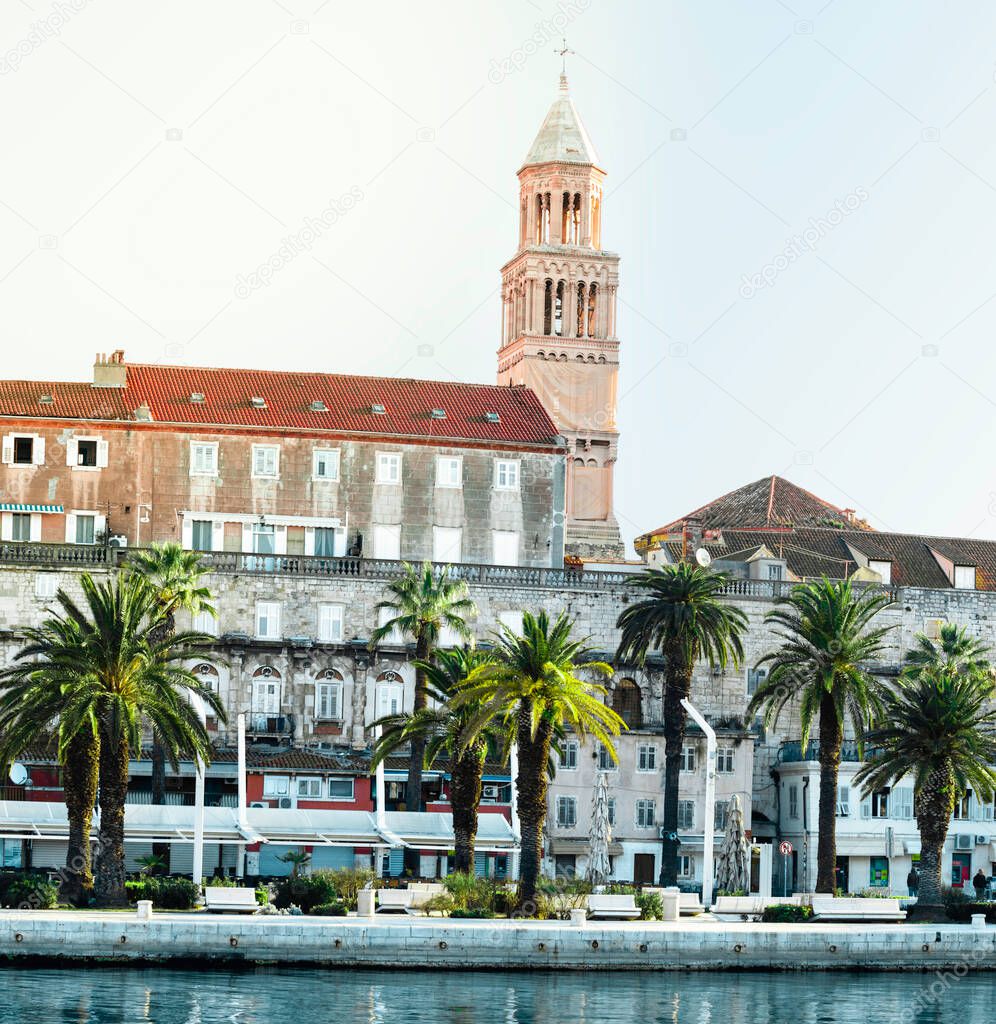 Riviera of the town of Split, Croatia. Green beautiful palm trees on the shore. Old belltower of saint dominus peeking above the old city buildings. Blue sea in the foreground