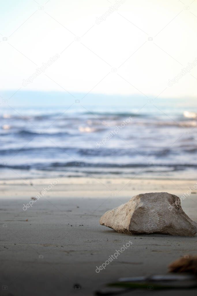Trapezoid shaped rock on a sandy beach of Bacvice in Split, Croatia. Blurred blue sea in the distance, blue sky and islands barely visible in the distance
