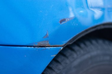 Halka açık bir otoparkta mavi bir arabanın tamponuna çizik. Şehir otoparkında nadir bir olay yeri değil. Çamurluk kazası ve hasarlı vücut boyası. Metal paslanıyor ve boya yok oluyor..