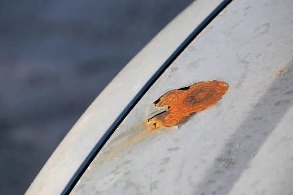 Big orange rust spot on the hood of a silver car. Peeled layer of paint enabling rust and corrosion to take effect on car body work.